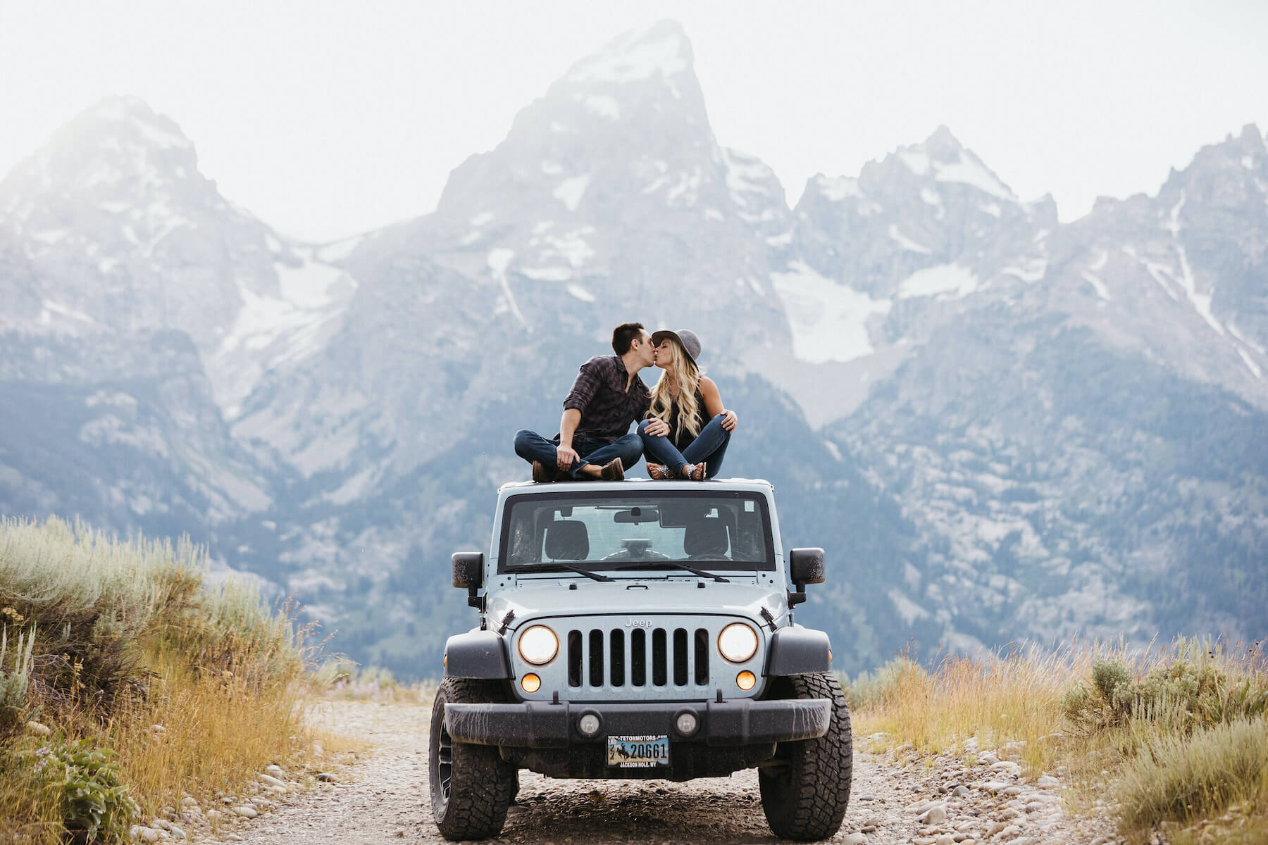 Couple hugging and sitting on a jeep in front of mountains in Jackson Hole