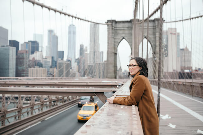 Woman smiling on a pedestrian walkway on the Brooklyn Bridge in New York City on a solo trip